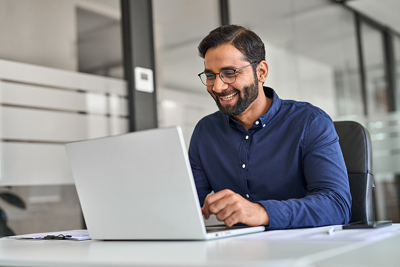 Professional Indian worker looking at laptop feeling happy with work result.